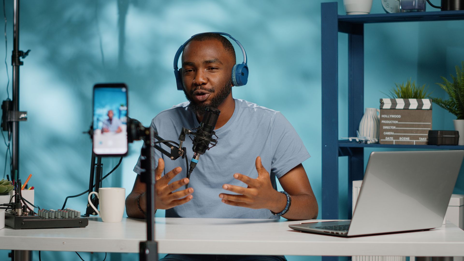 Man wearing headphones speaks into a microphone at a desk with a laptop, smartphone on tripod, and audio equipment, appearing to record or livestream content for Astoria Media Group’s SEO services.