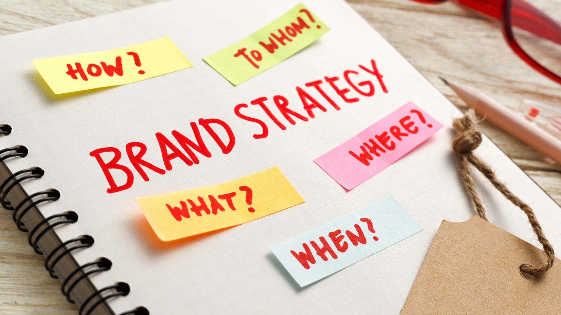 Notebook page with BRAND STRATEGY written in red, surrounded by sticky notes labeled How?, To Whom?, What?, Where?, and When?, reflecting the strategic planning process at Abilene Texas marketing agency Astoria Media Group.