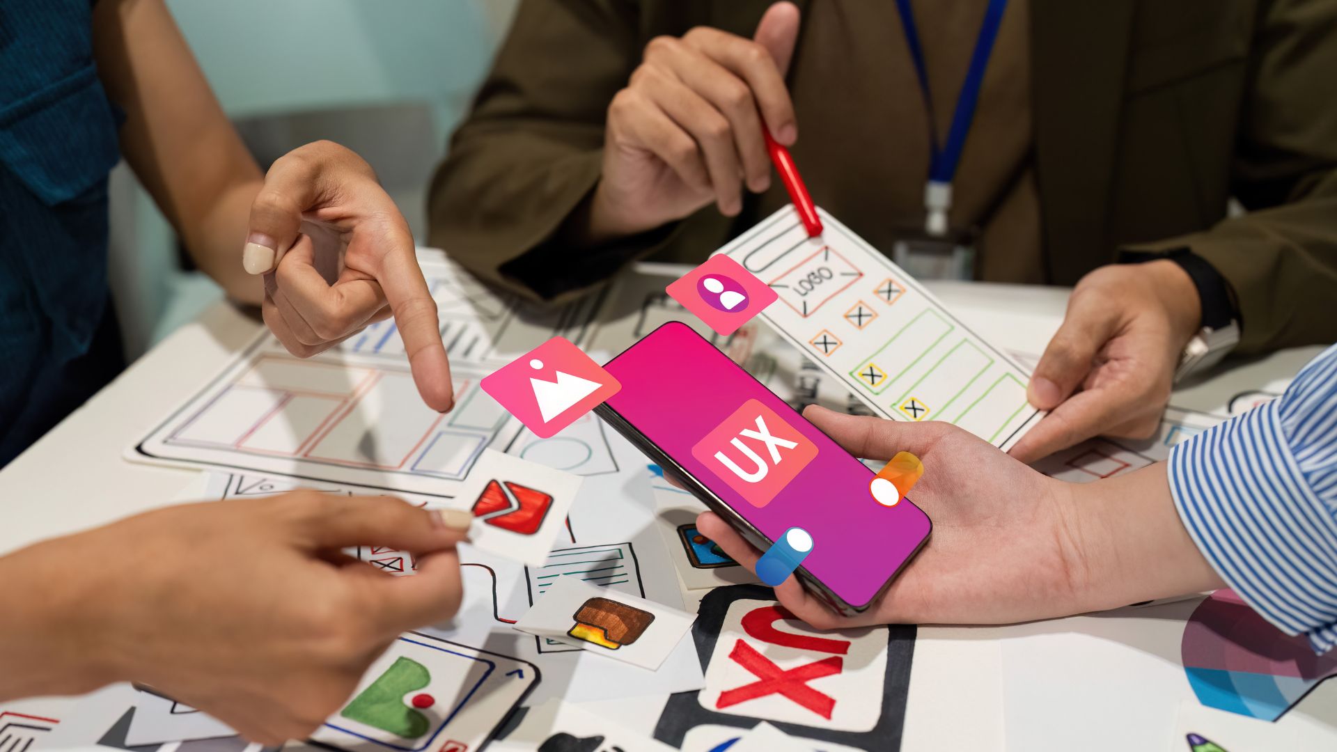 Three people collaborate on mobile app interface design, holding a smartphone and paper prototypes, with digital UX icons overlaid—showcasing Astoria Media Group’s expertise as a leading digital marketing agency.
