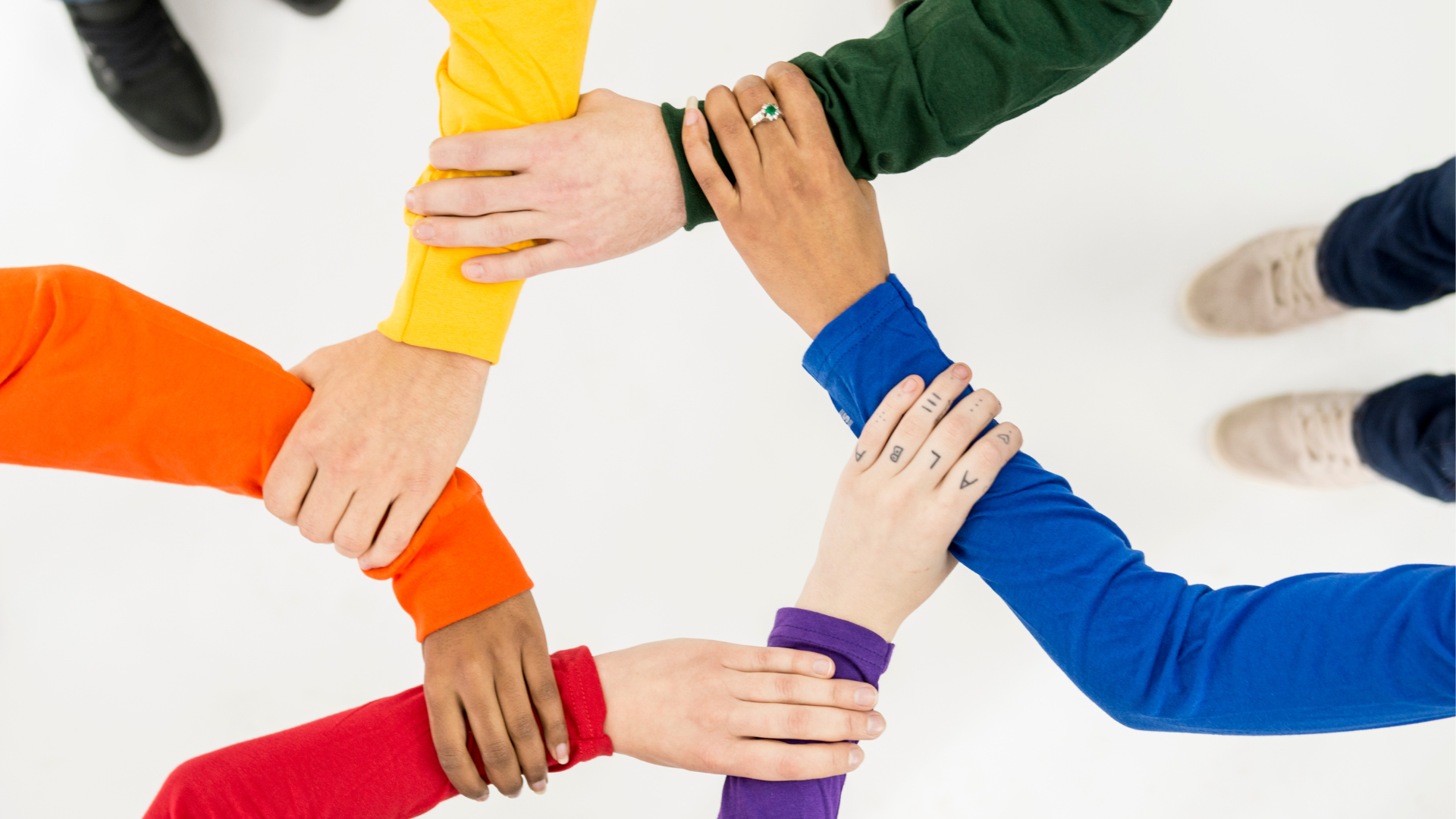 Six people in rainbow-colored long sleeves stand in a circle, each grasping the next's forearm, forming an interconnected chain—an image often used to symbolize teamwork in Abilene web design and WordPress development projects.